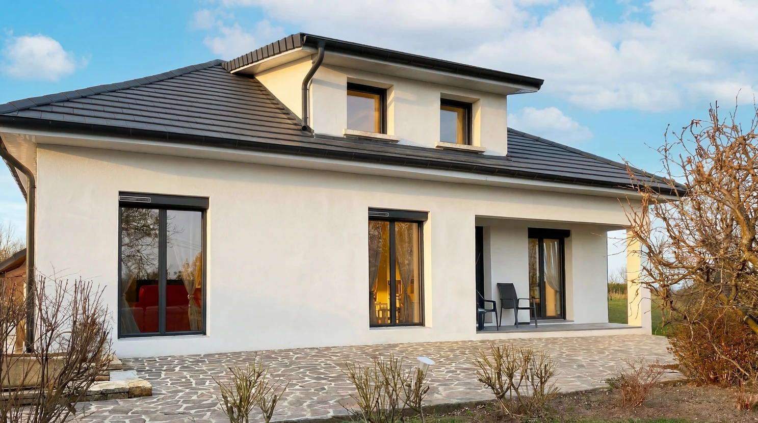Pergola bioclimatique à lames orientables en aluminium anthracite, adossée à une maison individuelle en crépi beige